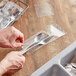 A hand putting a spoon in a plastic silverware bag.