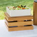 A Cal-Mil bamboo square crate riser holding a wooden tray with a bowl of salad.