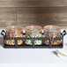 A black rustic jar condiment display with three jars of nuts on a table.
