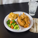 A Carlisle white melamine plate with broccoli and carrots and a clear plastic cup with a straw and ice on it.