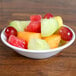 An Arcoroc Rondo fruit bowl filled with a variety of fruit on a table.