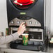 A person using a Bunn powdered cappuccino dispenser to pour coffee into a cup.