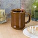 A Tuxton caramel mug on a table with coffee and a pastry.