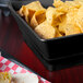 A black square basket with tortilla chips in it.