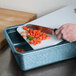 A person using an HS Inc. blue plastic tote to cut tomatoes on a cutting board.