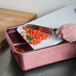 A person cutting tomatoes on a raspberry HS Inc. cutting board.