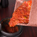 A container of salsa being poured into a bowl.