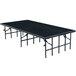 A National Public Seating portable stage with black legs and carpet on top.