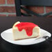 A slice of cheesecake with red sauce on a Tuxton white china plate.