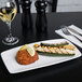 A rectangular white china plate with food and a lemon wedge on a table.