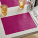 A wine colored scalloped paper placemat on a table with a glass of ice tea.