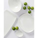A white Tuxton China ramekin on a white surface with a lime in it.