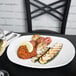 A white Tuxton china plate with food and a glass of wine on a table.
