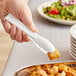A hand holding a white plastic tong over croutons.