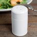 A close-up of a Tuxton white china pepper shaker on a table.