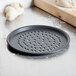 An American Metalcraft Super Perforated Hard Coat Anodized Aluminum Pizza Pan on a counter next to garlic.