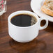 A Tuxton bright white china cup filled with brown liquid sits on a table.