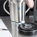 A person holding a stainless steel Waring 1 Qt. size adapter container.