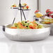 An American Metalcraft double wall hammered stainless steel bowl filled with fruit on a table.