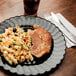 A Fineline Flairware black plastic plate of meat with a knife on a table.