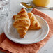 A Tuxton Concentrix white china plate with two croissants and a glass of orange juice.