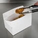 A person cutting up chicken in a white Take Out Lunch box.