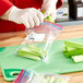 A person wearing gloves uses a knife to cut celery into a Ziploc bag.