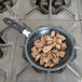 A Vollrath stainless steel frying pan with a black handle filled with meat on a stove.