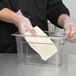 A person wearing gloves placing butter in a Cambro clear plastic food container.