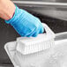 A hand in a blue glove using a Carlisle white hand scrub brush to clean a pan.