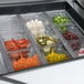 A Traulsen sandwich prep table with containers of food on a counter.