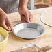 A round, shallow aluminum pie pan being held on a wooden surface.