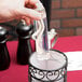 A hand holding a clear Sterno liquid wax tube over a glass container.