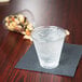 A Solo Ultra Clear PET plastic cup filled with water on a table next to a bowl of nuts.