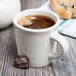 A Tuxton eggshell white china coffee mug filled with tea on a table with a tea bag.