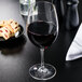 A Carlisle red wine glass filled with wine on a table next to a plate of cookies.