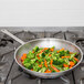 A Vollrath stainless steel fry pan filled with broccoli and carrots cooking on a stove.