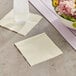 A customizable ivory beverage napkin next to a glass of water on a table with a bowl of flowers.