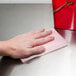 A hand using a Chicopee pink medium-duty towel to wipe a metal surface.