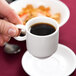 A person holding a white Arcoroc porcelain cup of coffee.