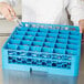 A person using a Carlisle glass rack to put a glass in a blue container.