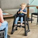 A black restaurant high chair with wheels, shown in use by a child at a dining table.