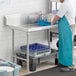 A man in a blue apron washing dishes on a Regency clean dish table.