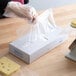 A person in gloves cutting cheese on a table using LK Packaging plastic deli wrap.