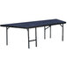 A National Public Seating portable stage pie unit with blue carpet on a rectangular table.