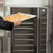 A person holding a tray of bread in a Metro C5 holding cabinet.