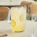 A clear Choice plastic beverage pitcher of lemonade with ice and lemon slices on a table.