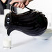 A hand holding a Vollrath black beverage server pouring milk into a glass.