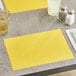 A yellow scalloped paper placemat on a table with a glass of liquid.