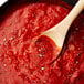 A wooden spoon in a bowl of red sauce with Regal Bulk Fancy Oregano Leaves on a white background.